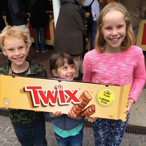 Three sneaky looking kids hold a huge twix chocolate bar.